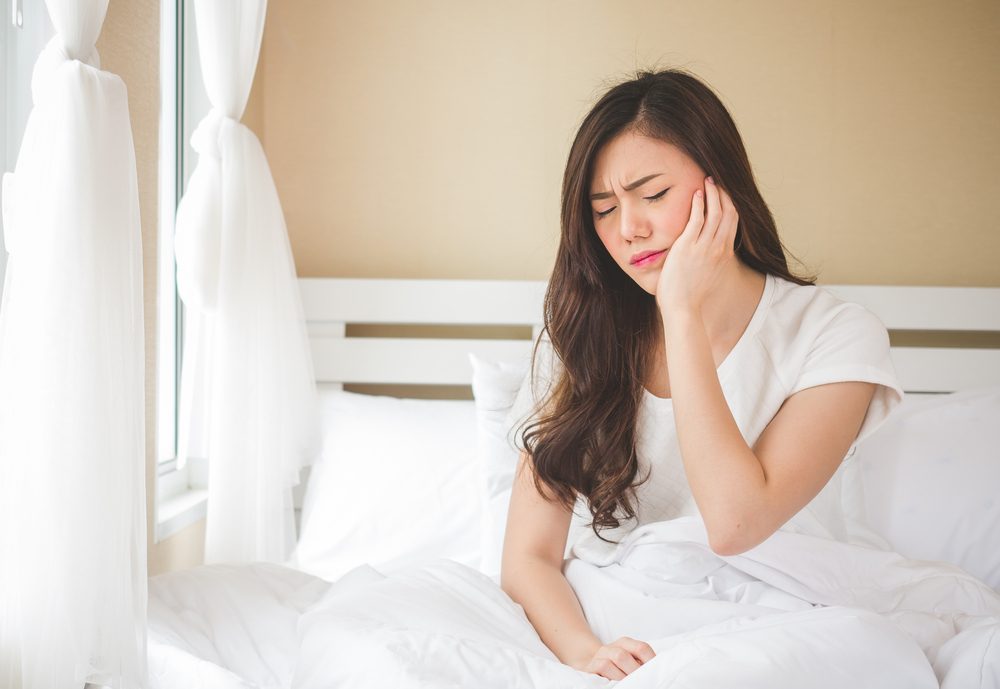 Woman holds her face due to jaw pain when waking up in the morning.