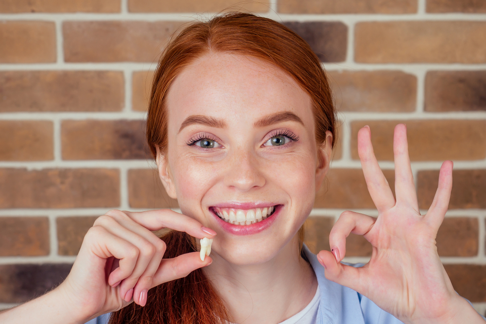 Woman holds a tooth and looks happy after recovering from tooth extraction.